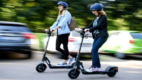 Two scooters being ridden with helmets in motion.
