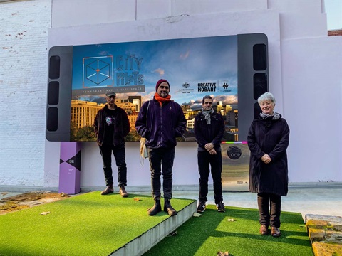 Artists David Campbell, Matt Daniels, Tom O'Hern, and Margaret Woodward standing in front of the City of Hobart LOOP screen in MidTown.