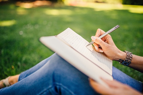 Unidentified individual sitting in a field writing in a notebook