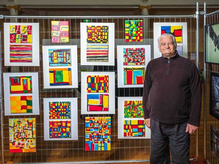 A man standing in front of a wire fence at City Hall with his coloured canvas art work hanging in the background A man standing in front of a wire fence at City Hall with his coloured canvas art work hanging in the background