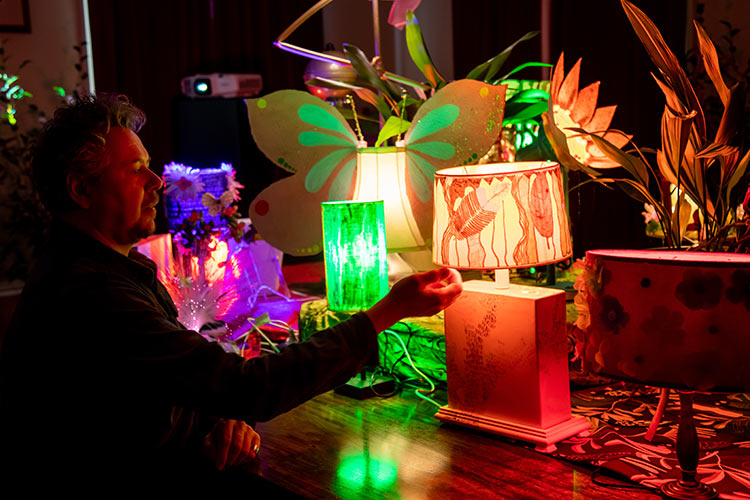 Colourful lamps displayed together with lead artist Alex Moss kneeling down turning on the lamp.