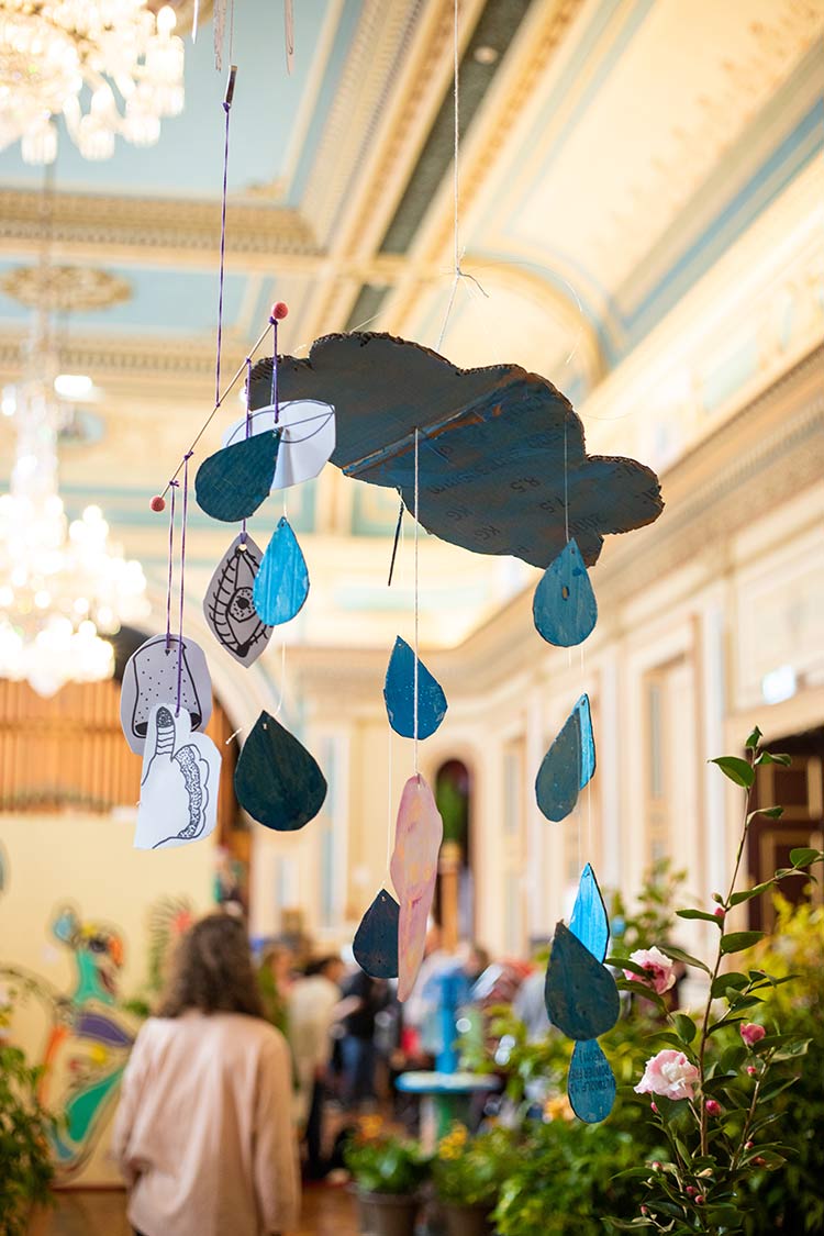 Hanging blue raindrops and hand drawn facial features suspended from a large blue cloud.