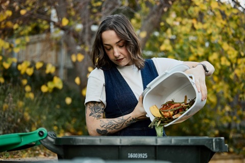 Person tipping food scraps from their kitchen caddy into their FOGO wheelie bin
