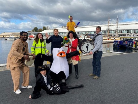 Image includes entertainers for Hobart's Long Waterfront Weekend including a juggler, two pirates, two drummers, a penguin, TasPorts, and Hobart's Lord Mayor Anna Reynolds.